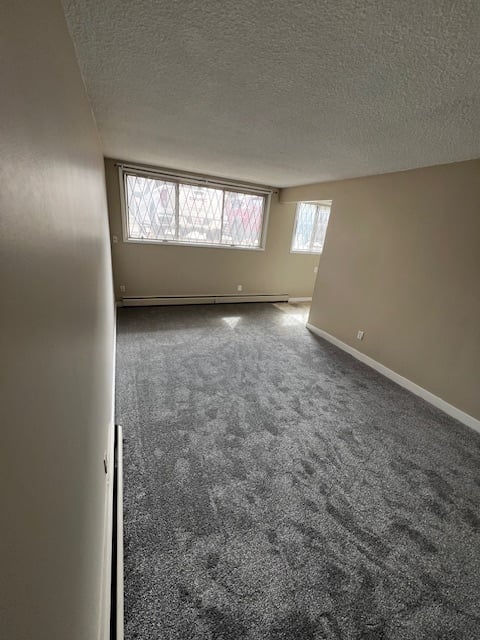 Empty apartment room with gray carpeting, beige walls, window with blinds, and textured ceiling