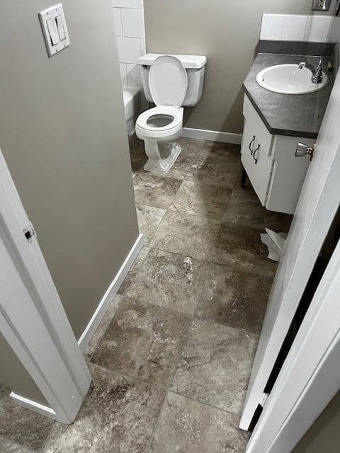 Small bathroom interior with toilet, sink vanity, concrete tile flooring, and white cabinetry